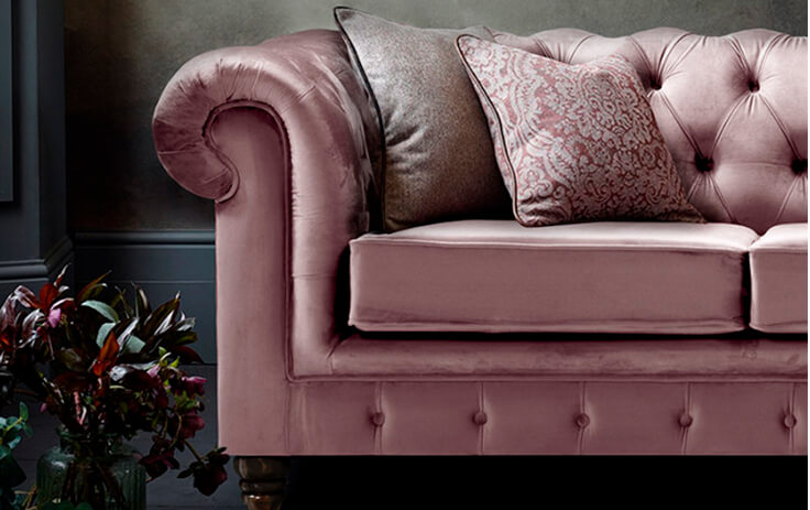 Velvet pink Chesterfield-style couch with two scatter cushions against a dark grey wall